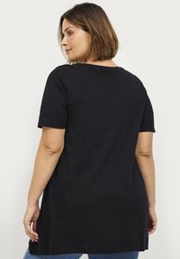 T-shirt nero a maniche corte realizzato in cotone morbido, con scollatura rotonda e orlo posteriore leggermente più lungo per un fit rilassato.