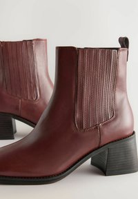 Botines de cuero marrón hasta el tobillo con paneles laterales elásticos, acentos texturizados, punta afilada y un tacón bloque medio. Acabado suave y costuras en contraste.