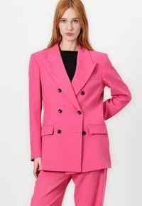 Double-breasted pink blazer made of textured fabric, featuring two side pockets, black buttons, and a sharp collar design.