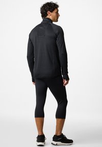 Zwarte sportjack met textuurstof en staande kraag, gecombineerd met zwarte capri-leggings en bijpassende sneakers.