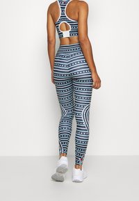 Set di top sportivo e leggings con motivi a righe blu scuro e bianchi con stelle. Il materiale ha una consistenza liscia; il design include un dettaglio con ritaglio.