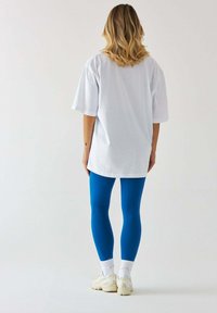 Luźna, biała bawełniana koszulka, w zestawieniu z jasnoniebieskimi legginsami i kremowymi sneakersami. Prosty, codzienny strój sportowy.