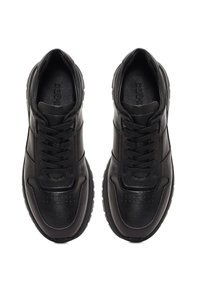 Par de zapatillas negras de cuero con cordones, suelas texturizadas y plantillas de marca, mostradas desde arriba sobre un fondo blanco.