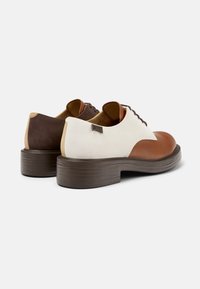 Scarpe in pelle marrone e bianca con punta rotonda, suola in gomma marrone testurizzata e tacco a contrasto. Presentano chiusura con lacci e dettaglio del logo.