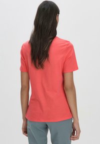 Korallinvärinen puuvillapaidan t-paita, jossa on lyhyet hihat ja pyöreä kaula-aukko, sileä pinta ja rento istuvuus. Yhdistetty harmaiden housujen kanssa.