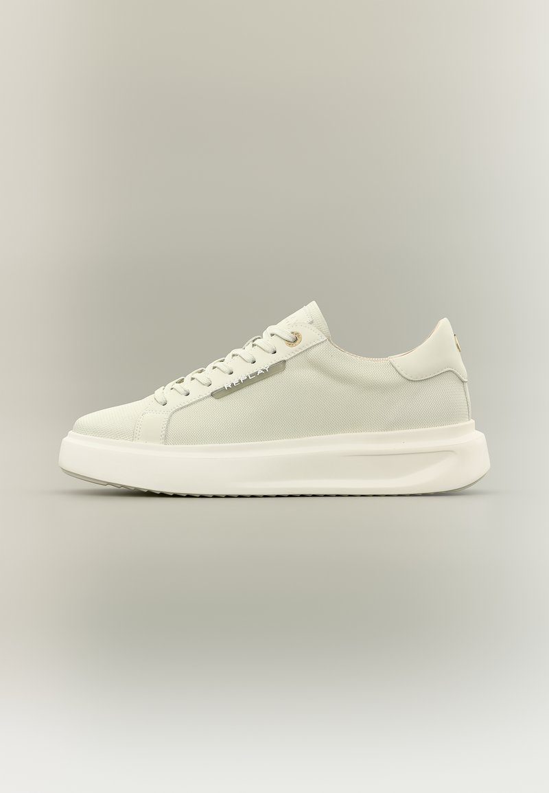 Baskets basses blanches avec dessus en toile, lacets à l'avant, semelle épaisse et étiquette en métal portant l'inscription "REPLAY" sur le côté.