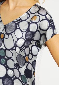 Korte mouwen blouse van een lichte stof met een meerkleurig cirkelpatroon op een grijze achtergrond, met een V-hals ontwerp en een zachte textuur.