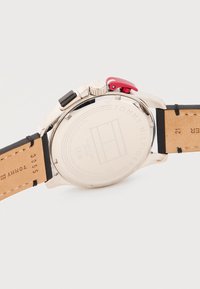 Πίσω μέρος ανδρικού ρολογιού Tommy Hilfiger από ανοξείδωτο ατσάλι με μπεζ δερμάτινα λουράκια, ανθεκτικό στο νερό έως 5 ατμόσφαιρες, εμφανίζει το λογότυπο της μάρκας και σειριακούς αριθμούς.