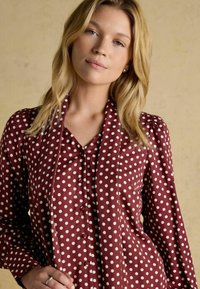 Maroon shirt with white polka dots, button-down front, and soft fabric. Features puffed sleeves and a V-neck design.