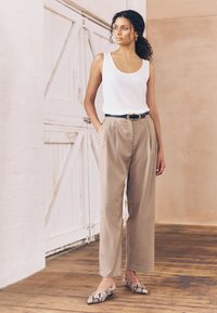 Hvid ribbet tanktop, beige plisserede bukser med en sort bælte, og mønstrede slip-on sko med slangeskindsdesign.