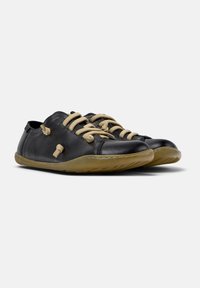Black leather shoes with beige laces, rounded toe, and flexible rubber sole. Features unique stitching details and minimalist design.