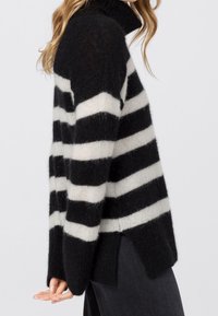 Pull à col roulé rayé noir et blanc en matière douce et duveteuse, avec des manches longues, une coupe décontractée et des fentes sur les côtés.