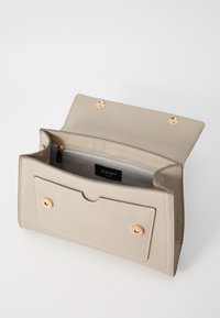 Beige læderhåndtaske med hardware i guldtoner, to magnetiske knapper og en lynlåslomme indeni. Synlig syning og et mærket interiør label.
