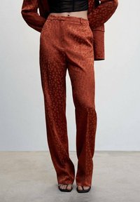 Pantalons de couleur rouille, à motif, avec une texture douce, présentant une coupe droite, des poches latérales et une taille mi-haute.