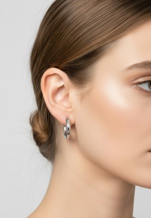 Boucles d'oreilles en argent avec une finition polie, présentant deux anneaux entrelacés, exposées sur l'oreille d'un modèle contre un fond neutre.