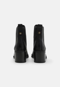 Bottines en cuir noir avec un talon carré, dotées d'une fermeture éclair et de coutures décoratives sur les côtés. Talon texturé pour une meilleure adhérence.