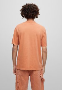 T-shirt in cotone color terracotta morbido, con maniche corte, scollatura a girocollo e vestibilità rilassata. Texture sottile visibile.