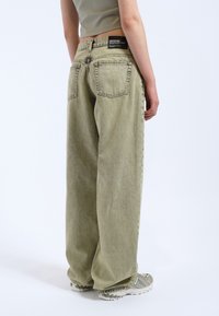 Jeans de pernera ancha en verde claro, fabricados en denim, con una cintura alta, grandes bolsillos traseros y una etiqueta negra en la cintura. Tejido texturizado.