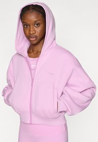 Ροζ φούτερ με φερμουάρ και κουκούλα, με άνετη εφαρμογή, μπροστινές τσέπες και κεντημένο λογότυπο "STRONGER". Ομαλή υφή και απαλό υλικό.