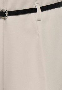 Pantalon beige au tissu lisse, équipé d'une ceinture noire avec une boucle en métal argenté et des passants pour un ajustement facile.