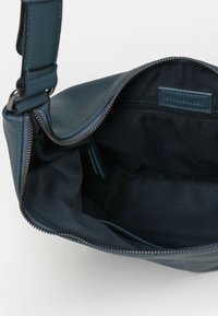 Ciemnoniebieska skórzana torebka z zamkiem błyskawicznym i materiałowym wykończeniem. Wewnątrz znajduje się kieszeń na zamek oraz małe przegródki do organizacji.