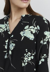 Svart blus med ett blommönster i ljusblått och vitt, med en knäppning framtill och en avslappnad passform. Mjuk och lätt tyg.