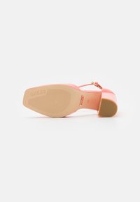 Tacco alto in pelle verniciata rosa con punta quadrata e cinturino alla caviglia regolabile. Presenta una suola in gomma beige testurizzata e il nome del brand impresso.