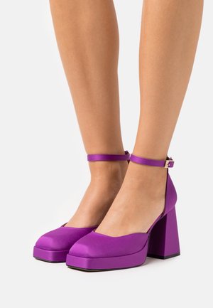 Fialové saténové platformové podpatky s kulatou špičkou, širokým blokovým podpatkem a páskem kolem kotníku s kovovou sponou. Hladký povrch.