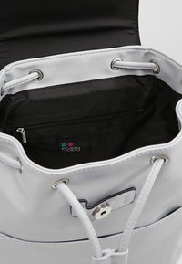 Borsa a secchiello in ecopelle grigia con fodera nera, chiusura con coulisse e tasca interna con zip. Presenta un'etichetta con il marchio e dettagli in metallo argentato.
