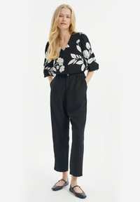 Zwarte bloemenblouse met witte patronen, relaxte pasvorm. Zwarte elastische taillebroek en platte, zwarte schoenen. Eenvoudig, elegant ontwerp met minimale details.