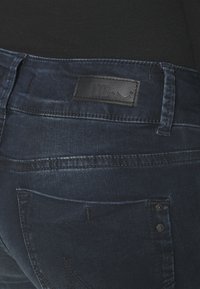 Mørk vaskede denimjeans med et lædermærke mærket "LTB," med et klassisk lomme-design og subtile falmede områder. Knapper er synlige.
