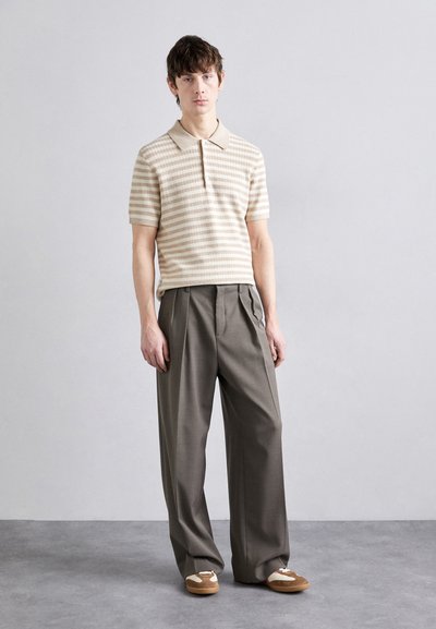 Beige pruhovaná polo tričko s krátkým rukávem spárované s vysokými šedými skládacími kalhotami a hnědými slip-on botami s krémovými akcenty.