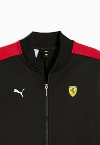 Sort zip-up jakke med røde skulderpaneler, der har et hvidt Puma-logo og et gult Ferrari-skjold på brystet. Teksturstof, ribbet krave.