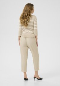Bežový pruhovaný top s dlhými rukávmi kombinovaný so svetložltými elegantnými nohavicami a čiernymi podpätkovými mules, s hladkým materiálom a skvele padnúceho strihu.