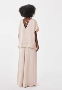Beige tweedelige outfit met een losse top met een V-achterkant en strikdetail, gecombineerd met wijde broekspijpen, beide gemaakt van een soepele stof.