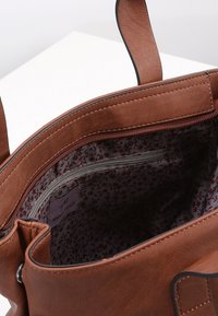 Bruine leren tas met een ritsvak en een voering van stoffen met bloemmotieven. Voorzien van stevige handvatten en een zachte textuur.