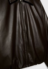 Gros plan d'une veste en cuir marron foncé avec une fermeture éclair à l'avant et un col, montrant une texture lisse et un léger éclat.
