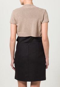 Ljusbrun kortärmad stickad tröja med stickad struktur och ribbad nederkant, ihopparad med en svart figurnära kjol.