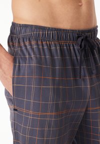 Navy pajama shorts with elastic waistband, orange and beige grid pattern, side pockets, and adjustable drawstring detail. Soft fabric texture.