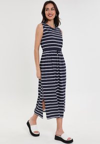 Navyblaue und weiße gestreifte ärmellose Midikleid mit elastischem Taillenbund, seitlichen Schlitzen, kombiniert mit weißen und schwarzen Plateau-Sandalen.