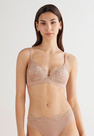 Lace bralette in nude with scalloped edges and thin straps; matching lace-trimmed panties; soft fabric and delicate floral pattern.