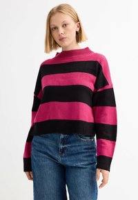 Suéter de punto recortado con amplias rayas negras y rosas, cuello acanalado alto y mangas sueltas. Combinado con jeans de tiro alto azules.