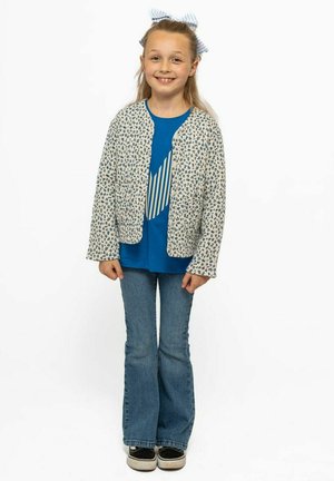 Blumenmuster-Kartoigan in hellem Creme über einem blauen T-Shirt mit einem weißen gestreiften Grafikdesign, kombiniert mit ausgestellten Jeans und schwarzen Turnschuhen.