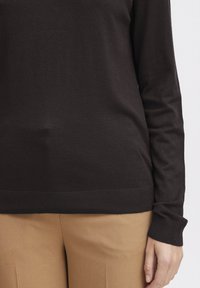 Haut en maille marron à manches longues avec un col rond et des poignets côtelés, associé à un pantalon en tissu marron clair. Texture lisse, design ajusté.