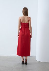 Punane satiinist midi kleit õhukeste rihmadega, figuuri rõhutav bodice ja varjatud selja tõmblukk, voolates otse allapoole sirgele servale. Mustad plokknõelad sandaalid.