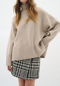 Beige stickad tröja med hög krage och ribbad nederkant, matchad med en kjol i svart och vitt hundtandmönster med texturerad tyg.