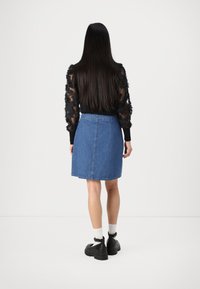 Denimskjørt i en mellomblå vask. A-linjefasong med slitt bak, satt sammen med en svart gjennomsiktig langermet topp og chunky svarte sko.