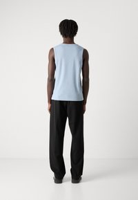 Haut sans manches bleu clair avec une texture côtelée, associé à un pantalon large noir. La tenue a un design minimaliste et une coupe décontractée.