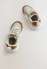 Baskets en cuir beige et marron avec des lacets blancs. Bout arrondi, détails perforés, col rembourré et semelle blanche avec des accents beiges.