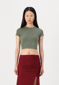 Oliven grønn cropped t-skjorte laget av ribbestrikket stoff med korte ermer, kombinert med en tettsittende burgunder skjørt med ruching og sidesplitter.